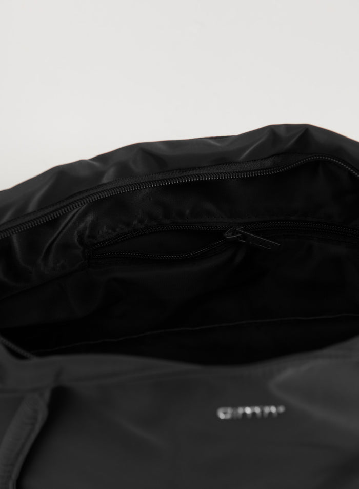 Mustan nylon-tote-laukun sisänäkymä, jossa vetoketjutasku ja hopeinen aim'n-logo.