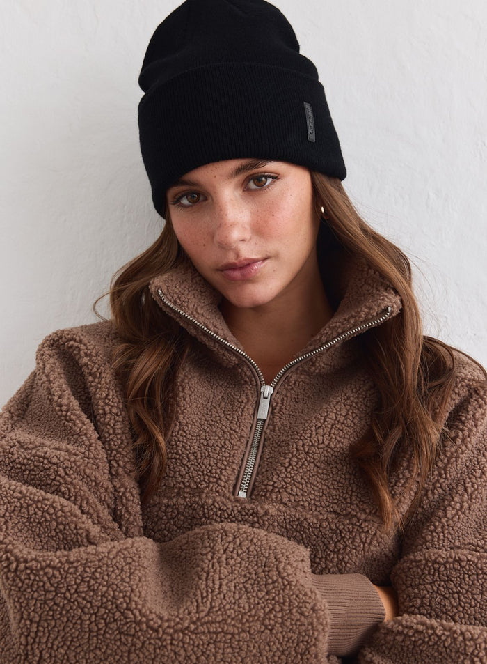 Musta ribbineulottu aim'n-outdoor-logopipo yhdistettynä pehmeään ruskeaan teddyfleeceen.
