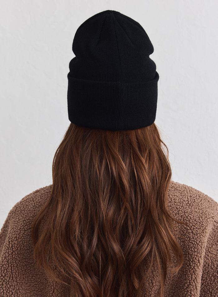 Musta neulottu aim'n Outdoor Logo Beanie takaapäin mallilla, jolla on ruskea fleecepaita.