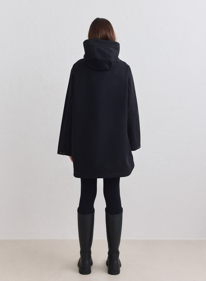 Musta vedenpitävä aim'n-hupputakki takaa kuvattuna minimalistisella mallilla ja kumisaappailla. [M-178cm]