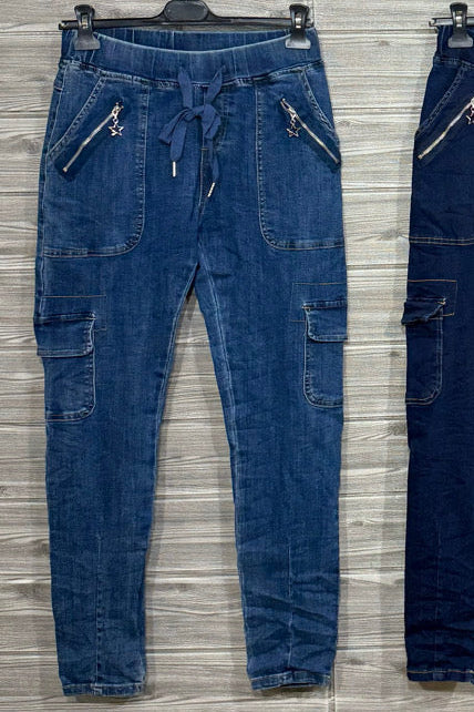 Blue denim jogger pants with patchwork panels, an elastic drawstring waist, cargo-style pockets, front zip pockets, and cuffed tapered hems.