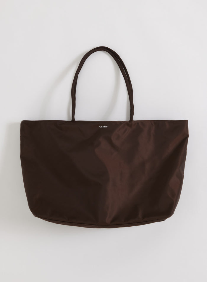 Tilava suklaanruskea nylon-viikonloppulaukku merkiltä aim'n kapeilla kahvoilla ja minimalistisella logolla.
