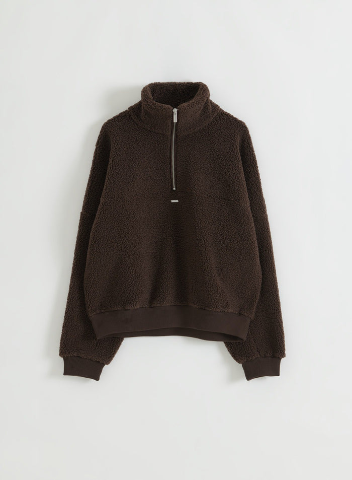 Suklaanruskea teddyfleece-pusero puolivetoketjulla aseteltuna tasolle