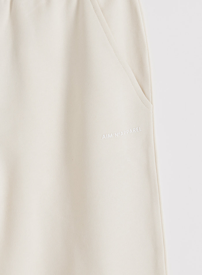 Yksityiskohta Cream Chunky Terry Sweatpants -housuista, joissa on sivutasku ja valkoinen aim'n-logo.