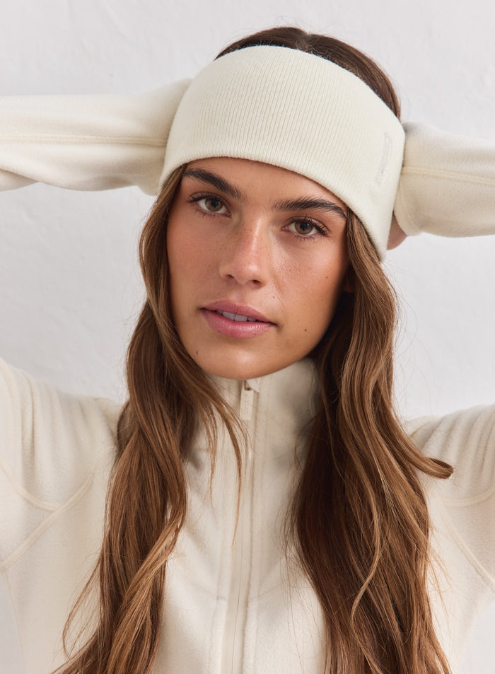 Nainen kermanvärisessä neulotussa aim'n Outdoor Logo Headband -pannassa ja yhteensopivassa fleecetakissa.