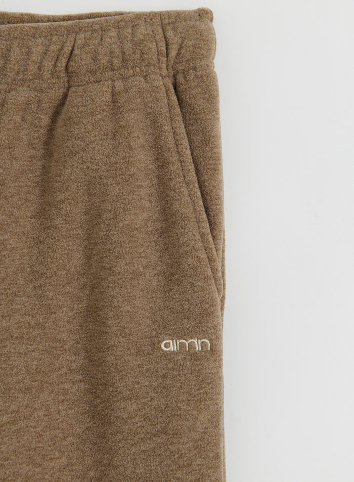 Lähikuva aim'n-merkkisistä hazelnut-värisistä fleece-housuista, jossa näkyy tasku ja logon yksityiskohta