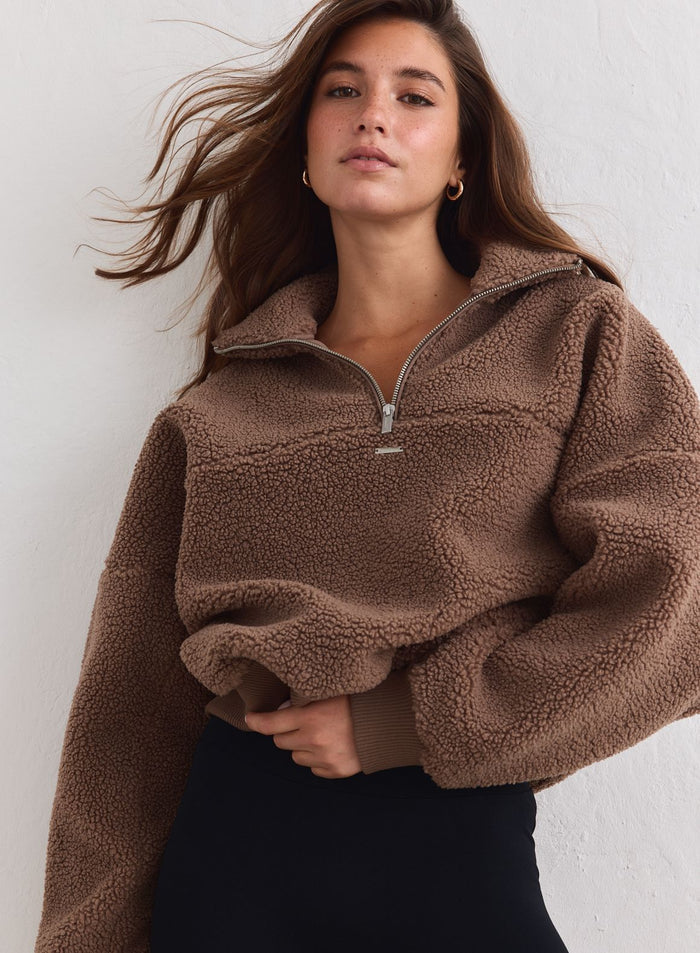 Nainen käyttää aim'n pähkinänruskeaa Pile Half Zip -paitaa pehmeästä fleecestä. [xs-178cm]