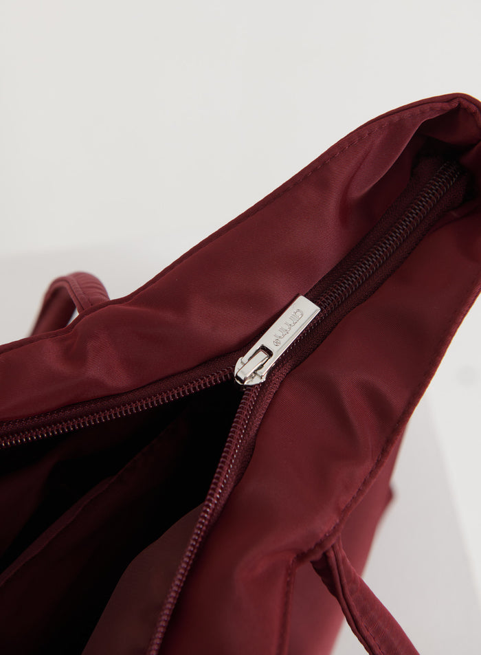 Lähikuva merlot-värisestä nylon-laukusta ja hopeisesta vetoketjusta aim'n-logolla.