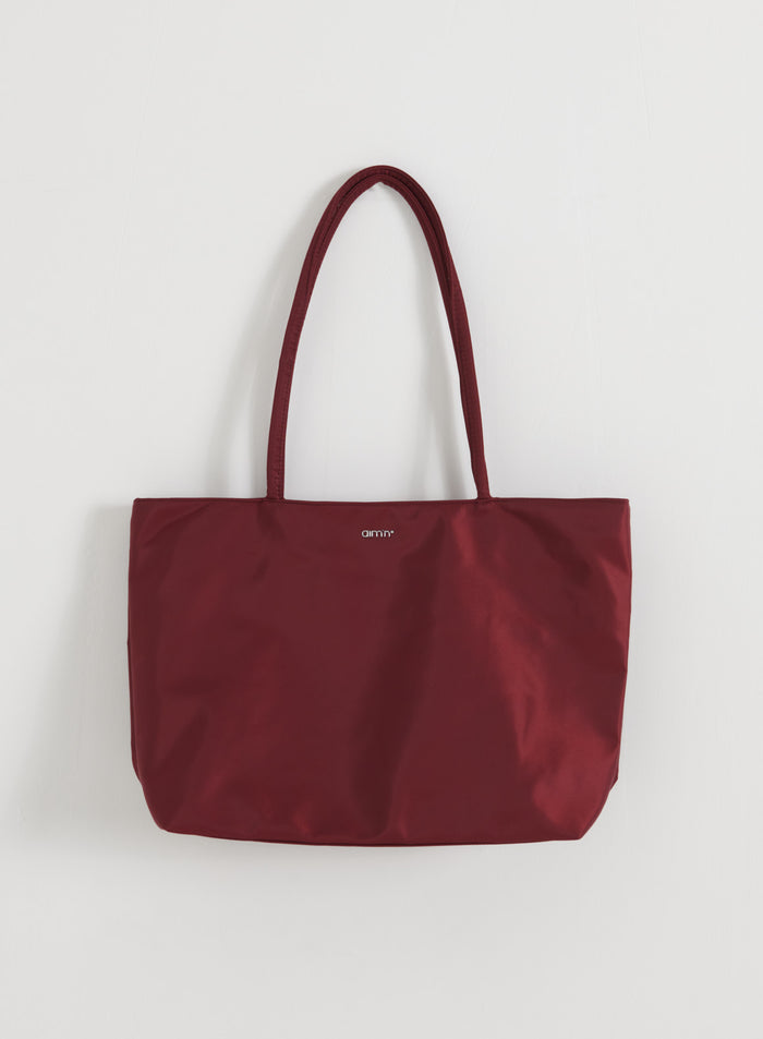 aim'n Merlot Nylon Tote Bag pitkillä olkahihnoilla ja pienellä logolla valkoisella taustalla.