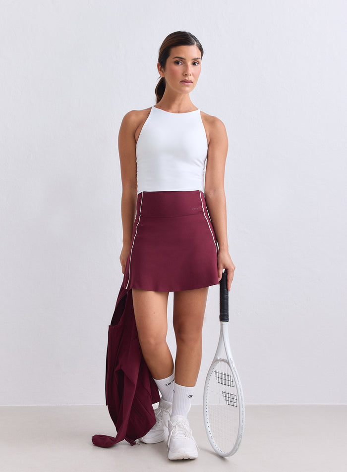 Merlot-värinen aim'n Sense Contrast Skort valkoisilla tereillä ja tennismailalla stailattuna. [XS-165cm]