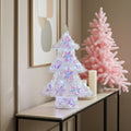 Decorative Christmas trees with colorful lights on a table against a neutral wall.