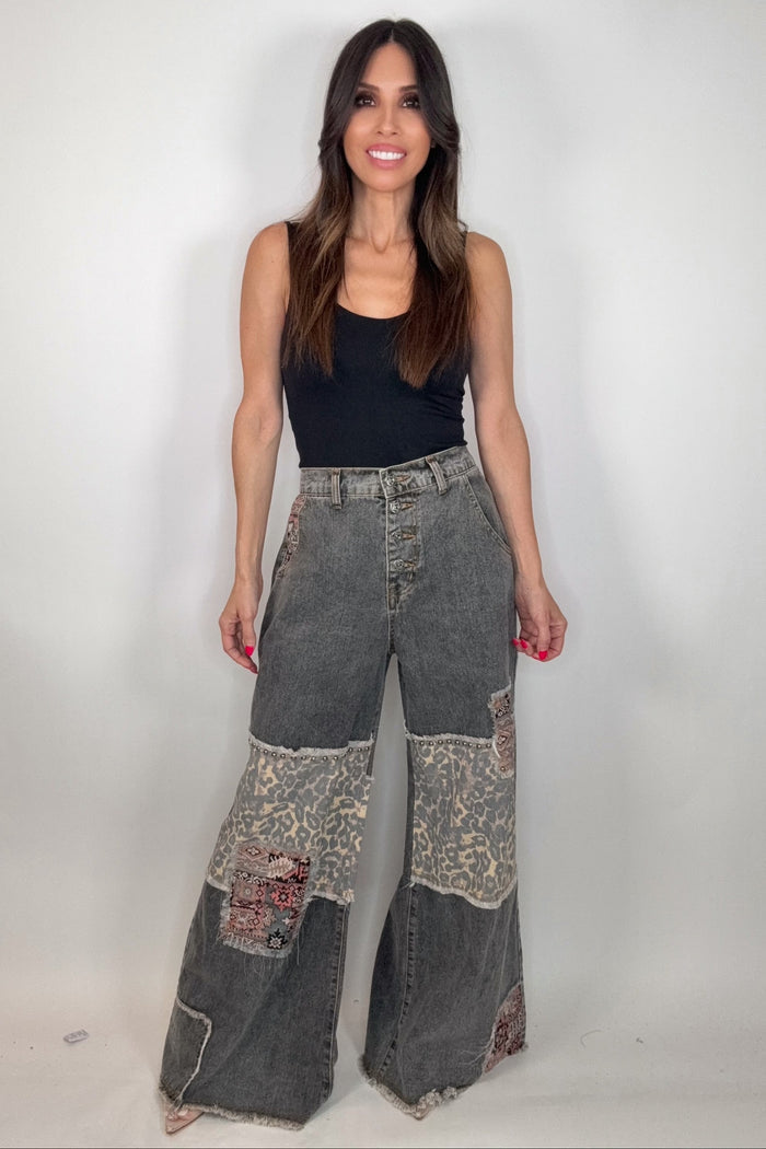 Black wide leg jeans with leopard print patchwork, contrast stitching, button fly detail, and a raw hem.