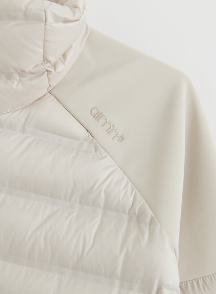 Lähikuva hiekanvärisestä Hybrid Jacket -takista, jossa näkyvät tikattu lämpöä eristävä paneeli, joustava hiha ja aim'n-logo