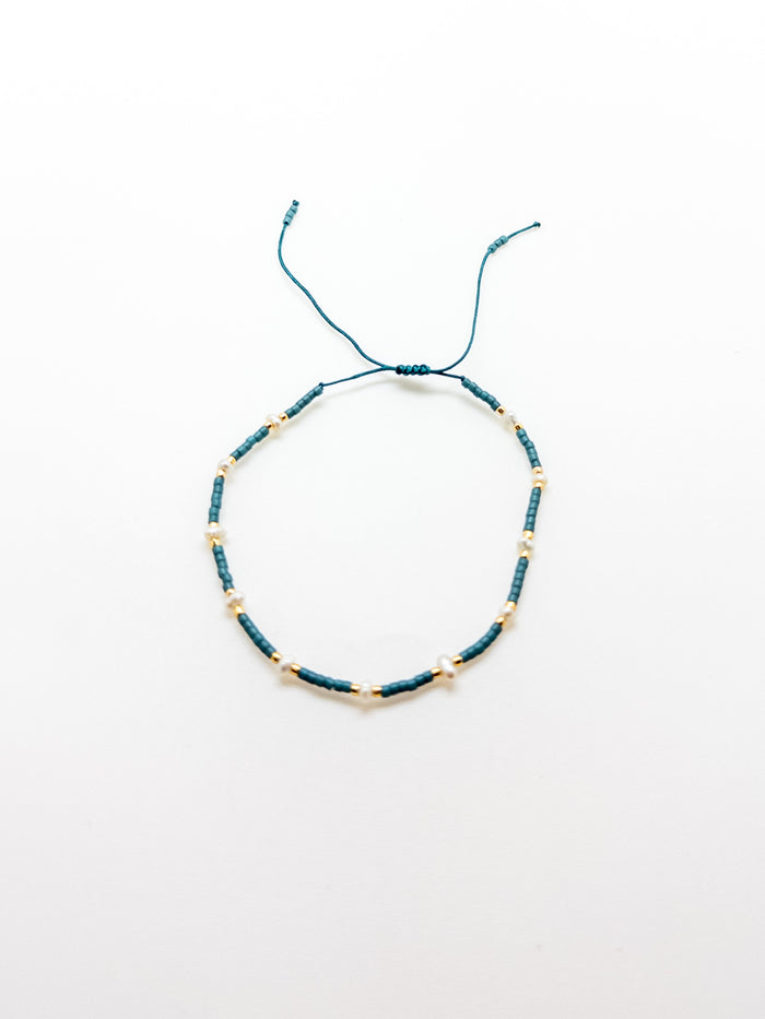 An adjustable teal bracelet with gold accents on a white background