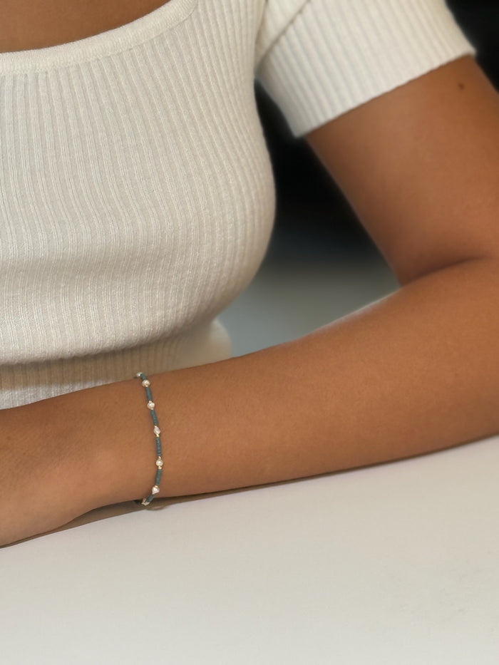 Teal beaded bracelet with gold and pearl accents showed on a models wrist